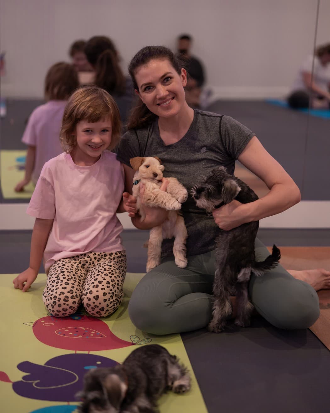A mother and daughter kneeling on a mat together, each holding a puppy after class