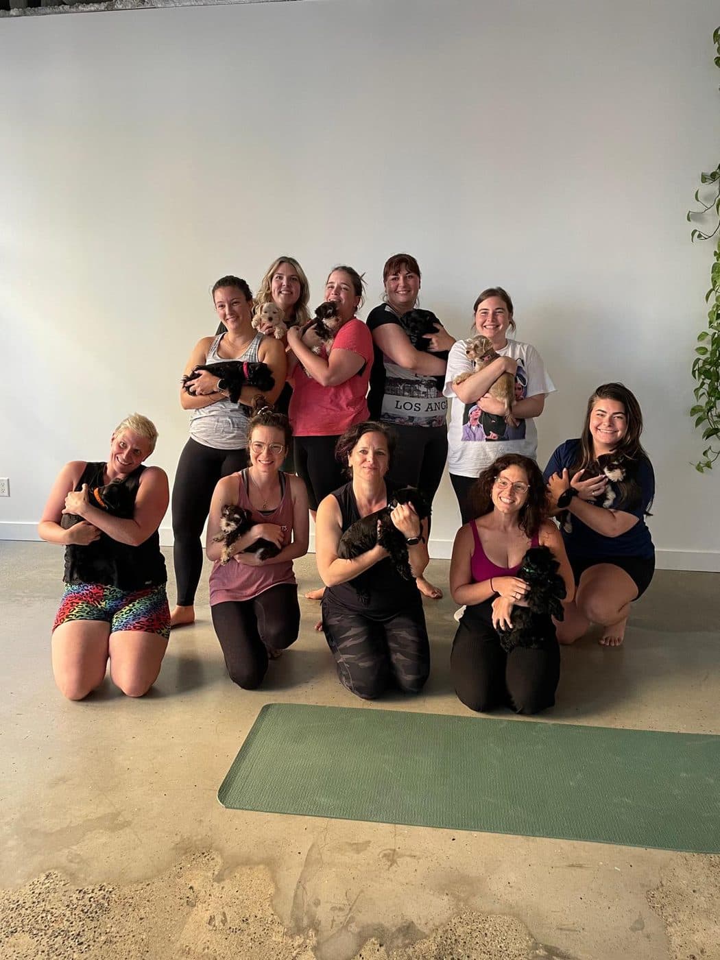 A group of students, each holding a puppy, posing together after a Puppy Yoga class
