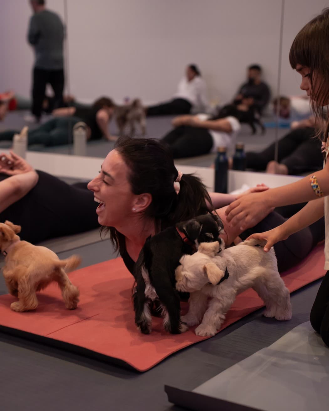 A student laughing on her mat while three puppies walk over her